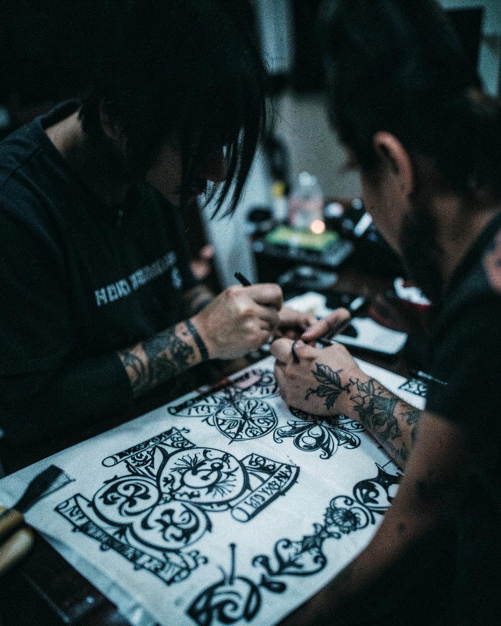 Tattoo artist Sable Vane at work over a blackwork flash sheet
